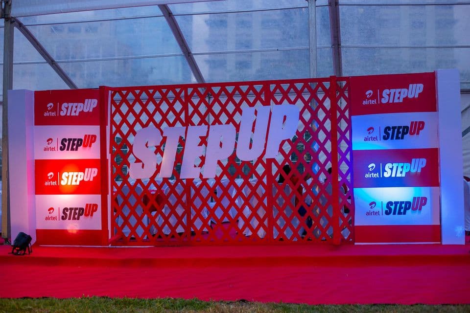Red lattice backdrop with repeated Airtel StepUp logos lit in blue and red